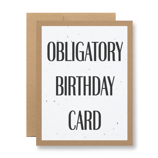 A My Store Plantable Greeting Card titled "Obligatory Birthday Card" features bold black lettering on handmade seed paper embedded with wildflower seeds, presented against a brown paper backdrop.