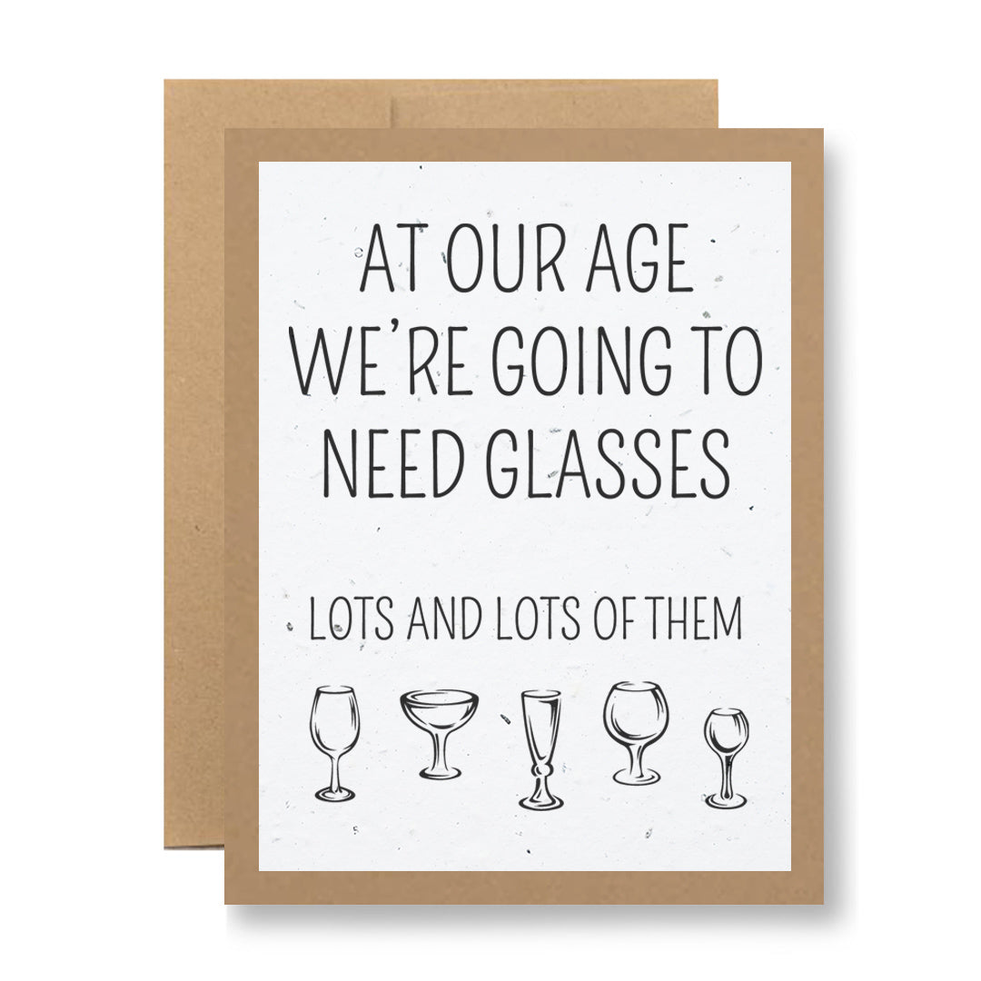 The Plantable Greeting Card by My Store is crafted on seed paper and features the text "At our age, we're going to need glasses..." alongside illustrations of an assortment of wine and cocktail glasses. Enjoy a touch of humor while planting wildflower seeds for a joyful surprise.