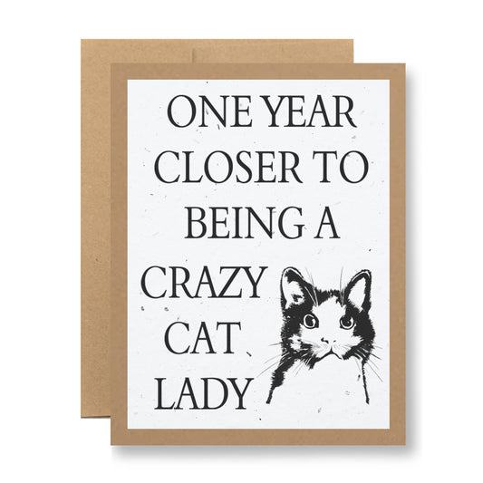 The Plantable Greeting Card from My Store features a cat illustration alongside the text "One year closer to being a crazy cat lady." This eco-friendly card is made on biodegradable material, offering a delightful mix of humor and sustainability against a simple backdrop.