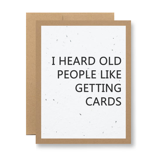 A greeting card from My Store, named "Plantable Greeting Card - I heard old people like getting cards," features a brown border with the humorous message, "I heard old people like getting cards." Made from biodegradable seed paper embedded with wildflower seeds, it offers a unique and eco-friendly touch. Another card is partially visible behind it.