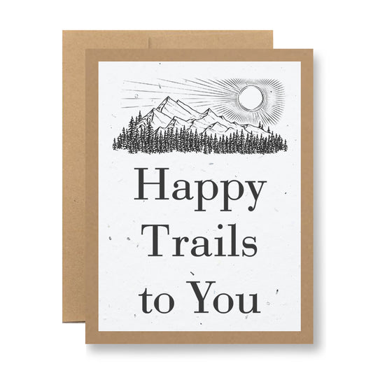 The "Plantable Greeting Card - Happy Trails to You" by My Store showcases the phrase "Happy Trails to You" on a white background. Above the text, it features illustrations of mountains, a sun, and pine trees, all crafted on seed paper that can be planted to cultivate wildflower seeds. The card is accompanied by a brown envelope.