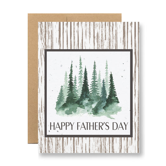 The Plantable Greeting Card - Happy Father's Day {forest} by My Store displays a watercolor illustration of evergreen trees on recycled cardstock. It features a rustic wooden pattern background with "Happy Father's Day" printed below the trees. The card comes with an envelope made from handmade seed paper, beautifully positioned behind it.