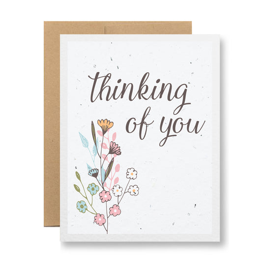 A "Plantable Greeting Card - Thinking of you {floral sketch}" by My Store, featuring elegant script text and crafted from handmade seed paper. The card showcases a colorful illustration of assorted flowers with a plain background, accompanied by a partially visible brown envelope that can bloom into wildflowers when planted.