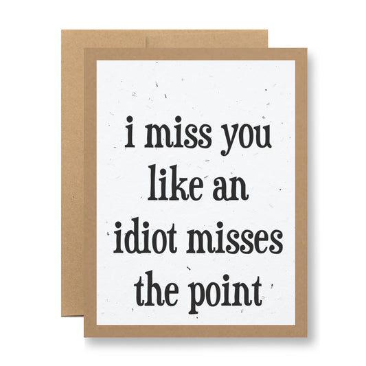 Introducing the "Plantable Greeting Card - I miss you like an idiot misses the point" by My Store: This eco-friendly card features bold black text with the humorous message "I miss you like an idiot misses the point," elegantly set against a white background with a brown border. Crafted from recycled cardstock, it adds a sustainable touch to your heartfelt sentiments.