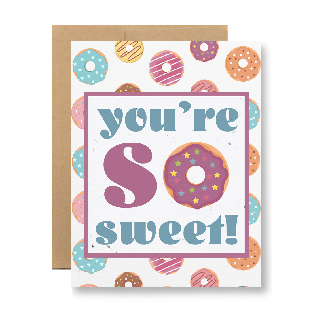 Presenting the "Plantable Greeting Card - You're so sweet!" by My Store, a specially crafted handmade card featuring vibrant donuts on its cover. The phrase "you're so sweet!" is highlighted with the O in "so" cleverly replaced by a donut. Made from seed paper, this card is paired with a brown envelope, allowing you to plant it and watch wildflower seeds bloom, spreading sweetness beyond words.