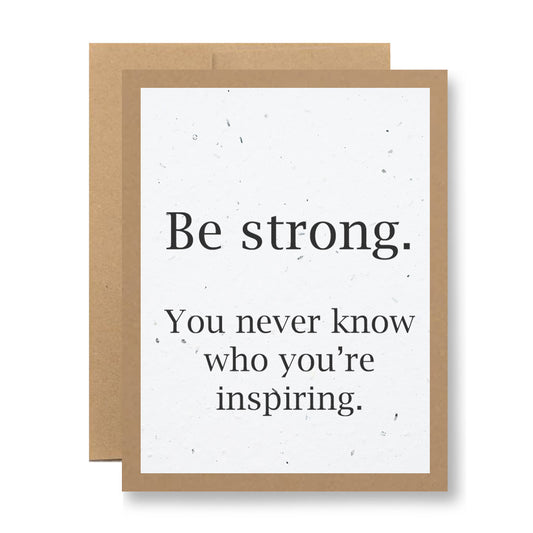 Introducing the "Plantable Greeting Card - Be strong. You never know who you're inspiring" by My Store. This card features a brown border and an inspirational message, crafted from handmade seed paper embedded with wildflower seeds. Its lightly speckled background offers an eco-friendly way to spread encouragement and positivity.