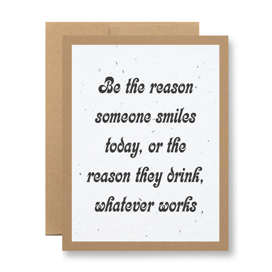 Handmade seed paper greeting card by My Store, featuring a humorous message in black cursive font: "Be the reason someone smiles today, or the reason they drink, whatever works." The card is bordered in brown and set against a plain backdrop, ready to grow wildflowers.