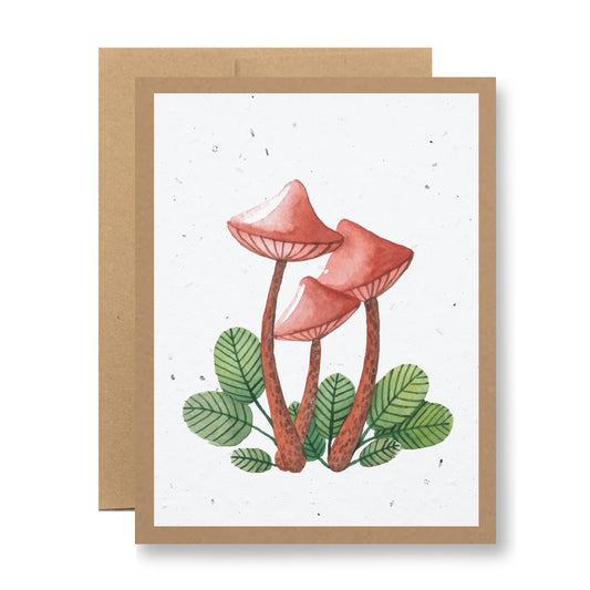 The "Plantable Greeting Card - watercolor mushrooms" from My Store features an illustration of three red-capped mushrooms with long, thin stems surrounded by green leaves on a speckled white background. Styled as a greeting card with a brown border and an envelope crafted from biodegradable paper, it's perfect for adding an eco-conscious touch.