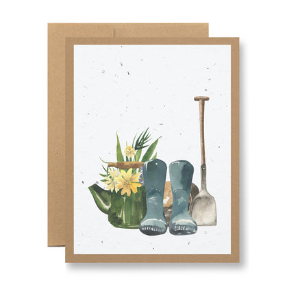 Plantable Greeting Card - {garden boots and shovel} by My Store: This illustrated card showcases a gardening scene with a watering can full of flowers, blue boots, and a shovel. Crafted from recycled cardstock, it features a neutral background framed with a brown border.