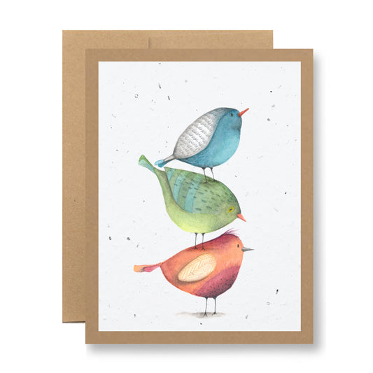 Introducing the "Plantable Greeting Card - {birds in a stack}" by My Store. This card showcases an illustration of three vibrant birds stacked vertically, with shades of blue, green, and red set against a cream-colored backdrop adorned with subtle speckles. Made from eco-friendly biodegradable card material or handmade seed paper, the card is accompanied by a brown envelope.