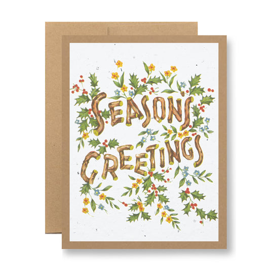 Introducing the Plantable Greeting Card - Season's Greetings {vintage woods} by My Store: This festive greeting card is crafted from seed paper and features the words "Season's Greetings" surrounded by holly leaves, red berries, and delicate yellow and blue flowers. With a white background framed by a brown border, this unique card transforms into wildflowers when planted.