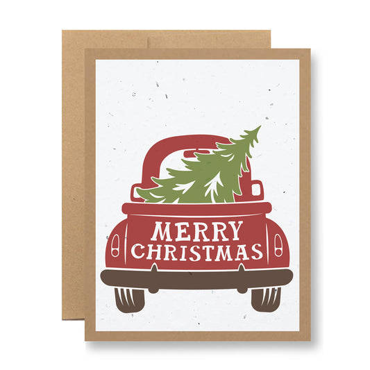 The Plantable Greeting Card - Merry Christmas {vintage truck} by My Store features a charming illustration of a red vintage truck adorned with a Christmas tree and packets of wildflower seeds in the back. The phrase "Merry Christmas" is inscribed on the truck, all set against a plain white background bordered in brown, capturing the simplicity and charm reminiscent of handmade cards.